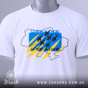 Футболка Україна авіація, біла, складена на поверхні, фон світло-сірий, принт з синім, жовтим та чорним кольорами, з контуром карти України та літаками, з біркою на комірці.