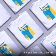 Футболка Україна Мати, біла, зображена на манекені, фон світло-сірий, принт з синьою статуєю та жовтим фоном, текст "Україна-Мати" чорним шрифтом.