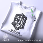 Футболка Україна починається з тебе. Біла футболка, складена на поверхні, з видимим принтом чорного кольору. На футболці видно етикетку з зеленим шнурком, що підкреслює стильний вигляд.