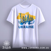 Футболка Україна тризуб, біла, підвішена на вішалці, фон світло-сірий, принт жовто-блакитний з тризубом та архітектурними елементами, текст 'UKRAINE' великими буквами.