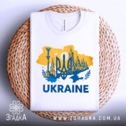 Футболка Україна тризуб, біла, зображена в плоскому вигляді на плетеній основі, фон натуральний, принт жовто-блакитний з тризубом та архітектурними елементами, текст 'UKRAINE' великими буквами.