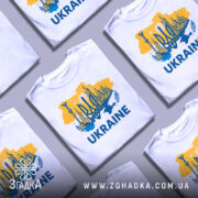 Футболка Україна тризуб, біла, зображена на манекені, фон світло-сірий, принт містить жовто-блакитну карту України з тризубом та архітектурними елементами, текст 'UKRAINE' великими буквами.