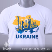 Футболка Україна тризуб, біла, зображена в плоскому вигляді, фон світло-сірий, принт жовто-блакитний з тризубом та архітектурними елементами, текст 'UKRAINE' великими буквами, на комірці є етикетка.