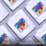 Футболка Україна білого кольору, зображена на манекені, з принтом червоних квітів на фоні синьо-жовтого кольору, ракурс спереду, фон нейтральний.