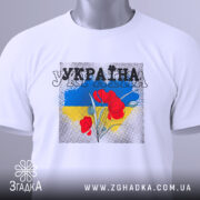 Футболка Україна білого кольору, складена на столі, з принтом червоних квітів на фоні синьо-жовтого кольору, ракурс зверху, видно етикетку з зеленим шнурком.