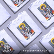 Футболка українка незламна, біла, зображена на манекені, фон світло-сірий, принт з жінкою в національному вбранні з автоматом, оточена вогнем і містом на задньому плані.