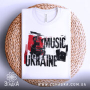 Футболка українська музика, біла, складена на плетеній кошику, фон світло-сірий, принт з гітарою та текстом 'MUSIC UKRAINE' у червоному та чорному кольорах.