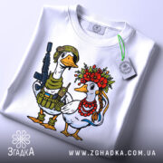 Футболка українська пара, біла, зображена зверху, фон світлий, принт з двома качками: одна в військовій формі з автоматом, інша в вінку з квітів та червоних намистин, на футболці є етикетка.