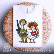 Футболка українська пара, біла, зображена зверху на плетеній основі, фон світлий, принт з двома качками: одна в військовій формі з автоматом, інша в вінку з квітів та червоних намистин.