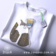 Футболка українська ППО білого кольору, складена на столі, ракурс зверху, фон світло-сірий, принт з малюнком літака та будинків у сірих тонах, текст "ППО" у блакитному кольорі, на комірці видна етикетка.