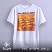 Футболка українське літо вареники, біла, підвішена на вішалці, фон світло-сірий, принт з варениками на решітці з сонцем на фоні.