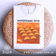 Футболка українське літо вареники, біла, складена на плетеній кошику, фон натуральний, принт з варениками на решітці з сонцем на фоні.