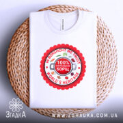 Футболка український борщ, біла, зображена зверху на плетеній основі, фон світло-сірий, принт круглий червоний з написами 'IN BORSCHT WE TRUST', '100% УКРАЇНСЬКИЙ БОРЩ' та 'WORLD'S HERITAGE', оточений малюнками овочів.