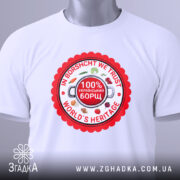 Футболка український борщ, біла, зображена зверху, фон світло-сірий, принт круглий червоний з написами 'IN BORSCHT WE TRUST', '100% УКРАЇНСЬКИЙ БОРЩ' та 'WORLD'S HERITAGE', прикріплена етикетка з зеленим шнурком.