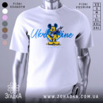 Футболка український дух, біла, зображена на манекені, фон градієнтний сірий, принт з мультяшним персонажем у жовтій та блакитній кольоровій гамі, напис 'Ukraine in my heart'.