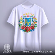 Футболка український герб, біла, зображена з фронтального ракурсу на вішалці, фон світло-сірий, принт містить герб України в синьому квадраті оточений кольоровими квітами.