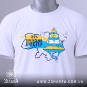 Футболка український хіпстер, біла, зображена зверху, фон світлий, принт з персонажем у жовто-блакитному вбранні, напис "100% українським хіпстер", на футболці є етикетка з зеленим шнурком.