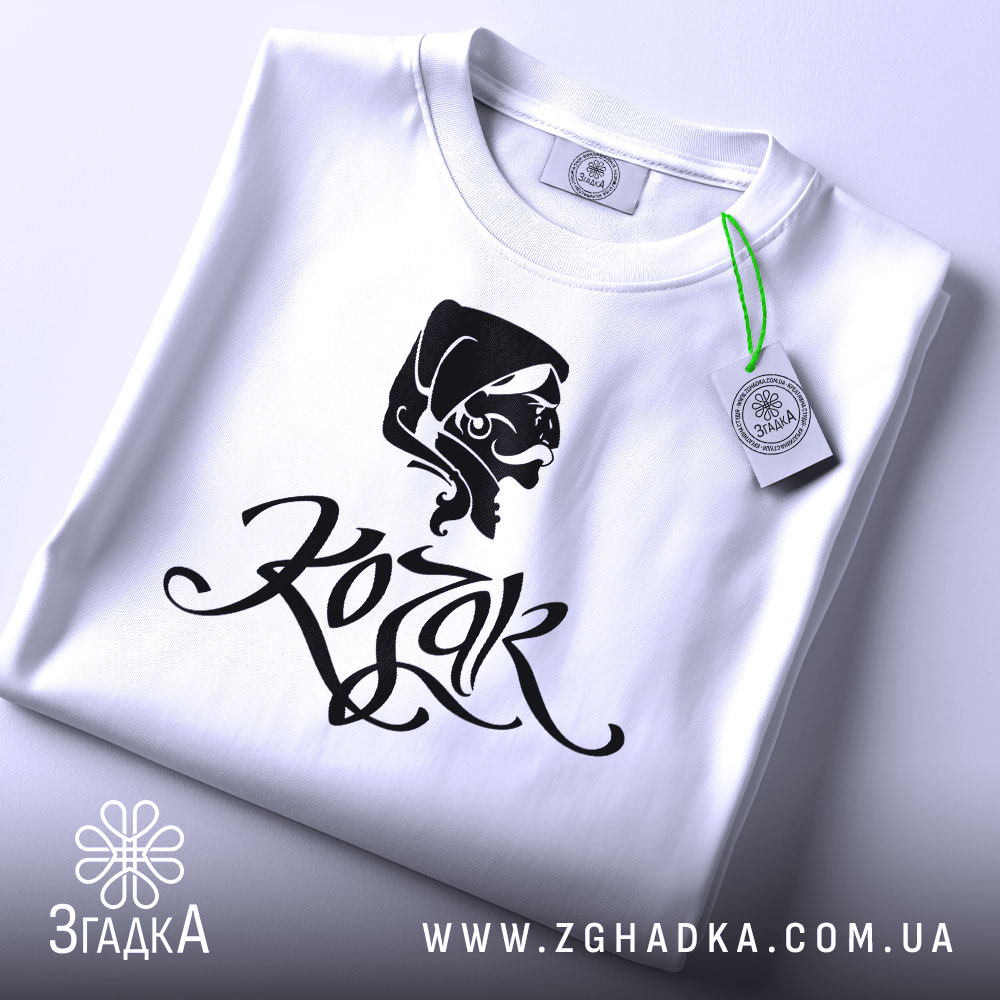 Футболка український козак, білого кольору, складена на поверхні, фон світло-сірий, принт з чорним малюнком козака та написом 'Kozak', на футболці є етикетка з зеленим шнурком.
