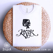 Футболка український козак, білого кольору, складена на плетеній основі, фон світло-сірий, принт з чорним малюнком козака та написом 'Kozak', видно округлий виріз горловини.