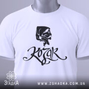 Футболка український козак, білого кольору, складена на поверхні, фон світло-сірий, принт з чорним малюнком козака та написом 'Kozak', на футболці є етикетка з зеленим шнурком.