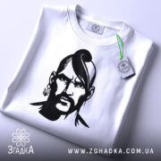 Футболка український козак, біла, зображена зверху, на ній є етикетка з зеленим шнурком, фон світло-сірий, принт чорного кольору з зображенням козака.