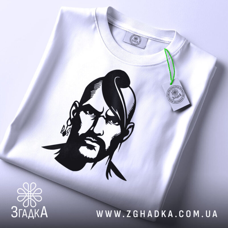 Футболка український козак, біла, зображена зверху, на ній є етикетка з зеленим шнурком, фон світло-сірий, принт чорного кольору з зображенням козака.