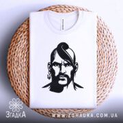 Футболка український козак, біла, складена на плетеній кошику, фон світлий, принт чорного кольору з зображенням козака з характерною зачіскою та серйозним виразом обличчя.