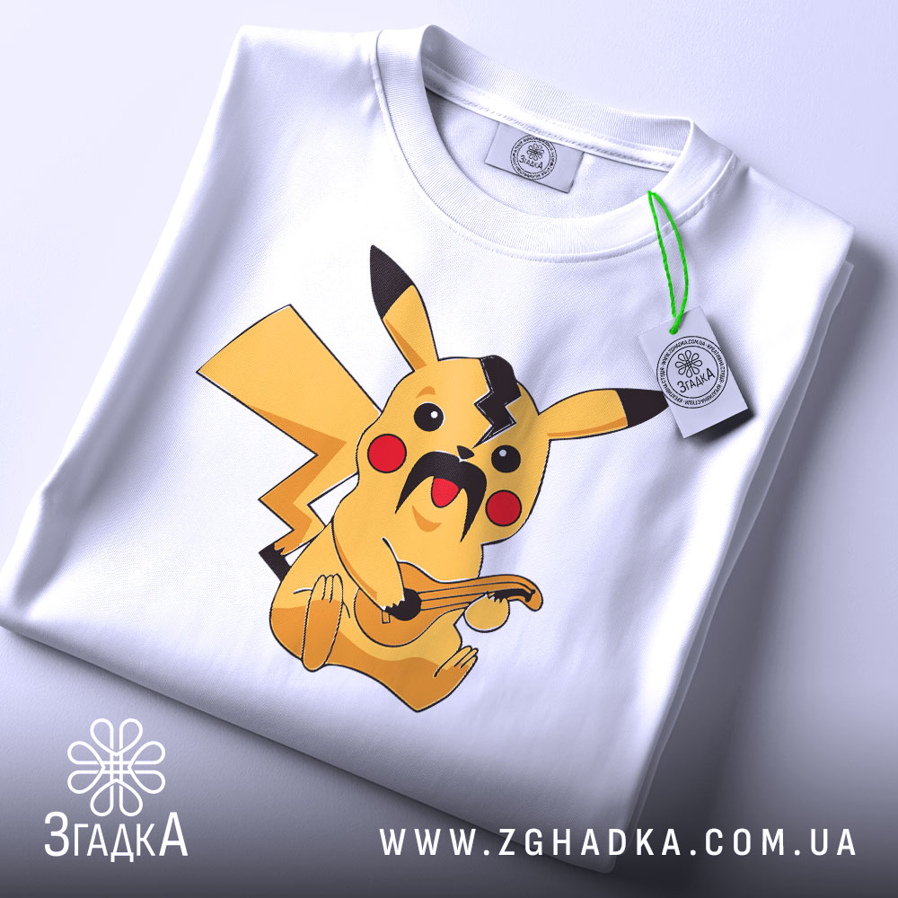 Футболка український пікачу, біла, складена на столі, фон світло-сірий, принт з жовтим пікачу з вусами та гітарою, на комірці є етикетка.