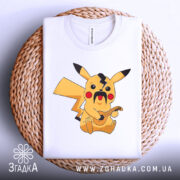 Футболка український пікачу, біла, складена на плетеній кошику, фон світло-сірий, принт з жовтим пікачу з вусами та гітарою.