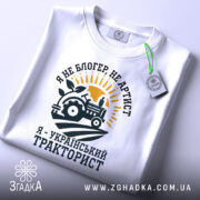 Футболка український тракторист, білого кольору, зображена в ракурсі зверху, фон світло-сірий, принт з трактором, сонцем і рослиною, текст чорного кольору, з етикеткою.
