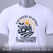Футболка український тракторист, білого кольору, зображена в ракурсі зверху, фон світло-сірий, принт з трактором, сонцем і рослиною, текст чорного кольору, з етикеткою.