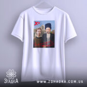 Футболка український вайб, біла, підвішена на вішалці, фон світло-сірий, принт зображує двох людей у традиційному одязі, текст "У український вайб" червоним кольором.