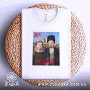 Футболка український вайб, біла, складена на плетеному кошику, фон нейтральний, принт містить зображення двох людей у традиційному одязі, текст "У український вайб" червоним кольором.