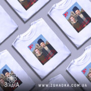 Футболка український вайб, біла, зображена на манекені, фон нейтральний, принт містить зображення двох людей у традиційному одязі на фоні будинку, текст "У український вайб" червоним кольором.