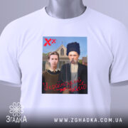 Футболка український вайб, біла, складена на столі, фон світлий, принт зображає двох людей у традиційному одязі, текст "У український вайб" червоним кольором, на футболці є етикетка з логотипом.