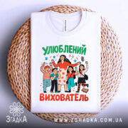 Футболка улюблений вихователь, білого кольору, зображена на плетеній основі, фон світлий, принт з персонажами, що святкують, з яскравими кольорами та написом 'Улюблений вихователь'.