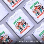 Футболка улюблений вихователь, білого кольору, зображена на манекені, фон світло-сірий, принт з веселими персонажами, що святкують, з яскравими кольорами та написом 'Улюблений вихователь'.