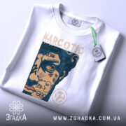 Футболка урбан стиль, біла, складена на поверхні, фон світло-сірий, принт з обличчям, що має графіті та напис "NARCOTIC", з зеленим ярликом.