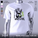 Футболка урбан стиль, біла, зображена з правого ракурсу, фон нейтральний, принт з чорним смайлом з вухами зайця, зеленими краплями фарби та написом 'NEW YORK'.