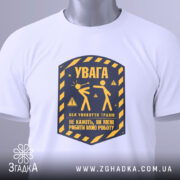 Футболка увага про роботу, біла, складена на поверхні, фон світло-сірий, принт у жовто-синіх тонах з написом 'УВАГА' та ілюстрацією двох фігур, з етикеткою на рукаві.