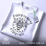 Футболка в кого бджоли, біла, зображена зверху, складена з етикеткою, фон світлий, принт з бджолою та написом вгорі і внизу.