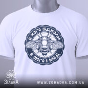 Футболка в кого бджоли, біла, складена на поверхні, з видимим етикеткою, фон світлий, принт з бджолою та написом у темно-синьому кольорі.