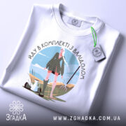 Футболка в комплекті з валідолом, білого кольору, зображена з верхнього ракурсу на столі, фон світлий, принт з дівчиною в зеленій сукні, прикрашений елементами природи.