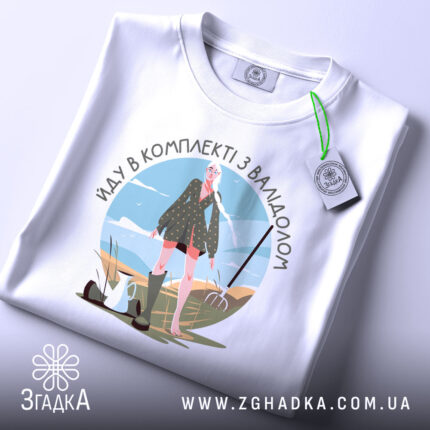 Футболка в комплекті з валідолом, білого кольору, зображена з верхнього ракурсу на столі, фон світлий, принт з дівчиною в зеленій сукні, прикрашений елементами природи.
