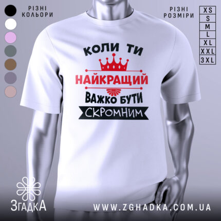 Футболка важко бути скромним. Біла футболка з коротким рукавом, зображена з правого ракурсу на манекені. На фоні світло-сірий градієнт. Принт чорного та червоного кольорів з текстом та короною.