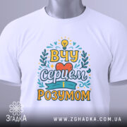 Футболка вчу серцем, білого кольору, зображена зверху, на плоскій поверхні, фон світло-сірий, принт з написом 'ВЧУ СЕРЦЕМ І РОЗУМОМ' в яскравих кольорах, з етикеткою на комірці.