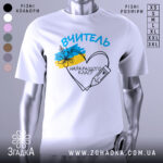 Футболка вчитель найкращого класу білого кольору, зображена з близького ракурсу на манекені, фон світло-сірий, принт містить напис 'ВЧИТЕЛЬ' та малюнок серця з олівцем і квітами в кольорах українського прапора.