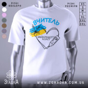 Футболка вчитель найкращого класу білого кольору, зображена з близького ракурсу на манекені, фон світло-сірий, принт містить напис 'ВЧИТЕЛЬ' та малюнок серця з олівцем і квітами в кольорах українського прапора.