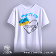 Футболка вчитель найкращого класу білого кольору, зображена з фронтального ракурсу на вішалці, фон світло-сірий, принт містить напис 'ВЧИТЕЛЬ' та малюнок серця з олівцем і квітами в кольорах українського прапора.