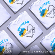 Футболка вчитель найкращого класу білого кольору, зображена з близького ракурсу на манекені, фон світло-сірий, принт містить напис 'ВЧИТЕЛЬ' та малюнок серця з олівцем і квітами в кольорах українського прапора.